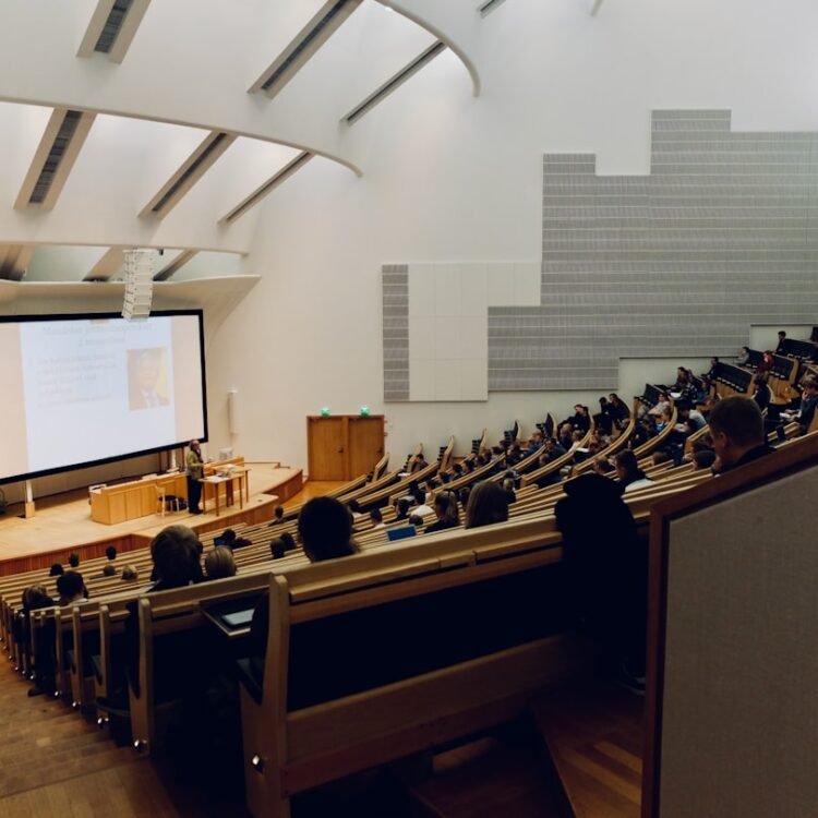 Sala de aula universitária moderna com alunos usando laptops e quadro digital ao fundo.
