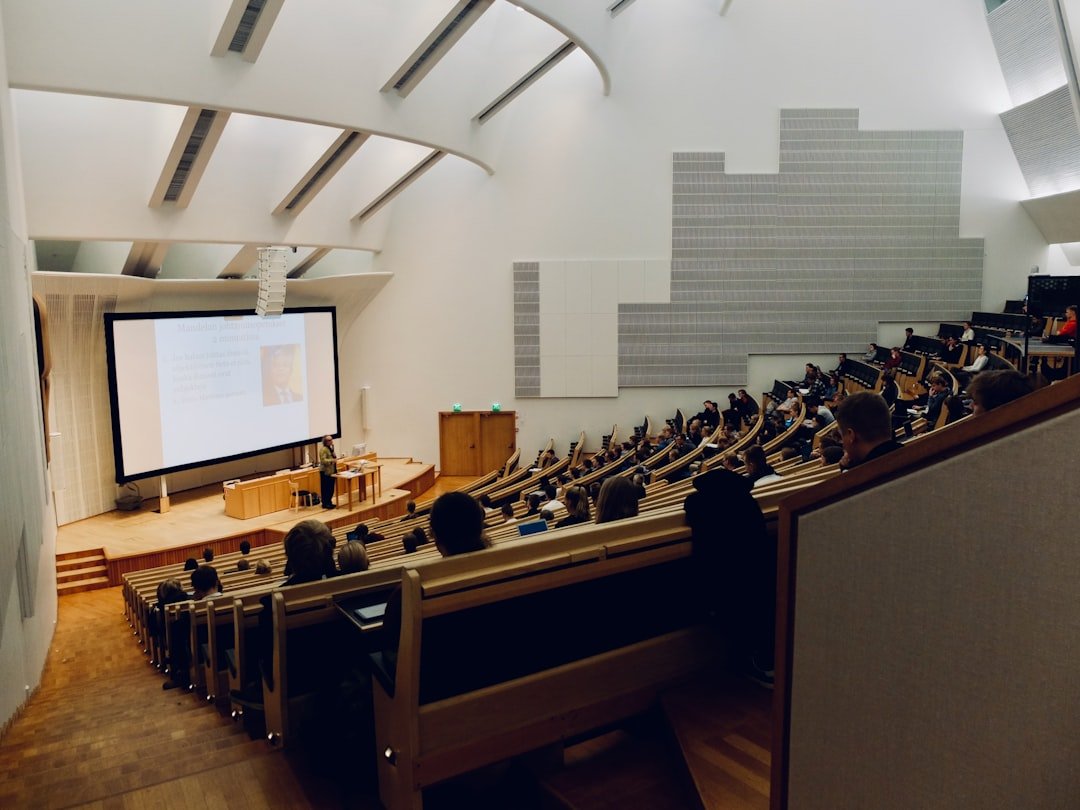 Sala de aula universitária moderna com alunos usando laptops e quadro digital ao fundo.